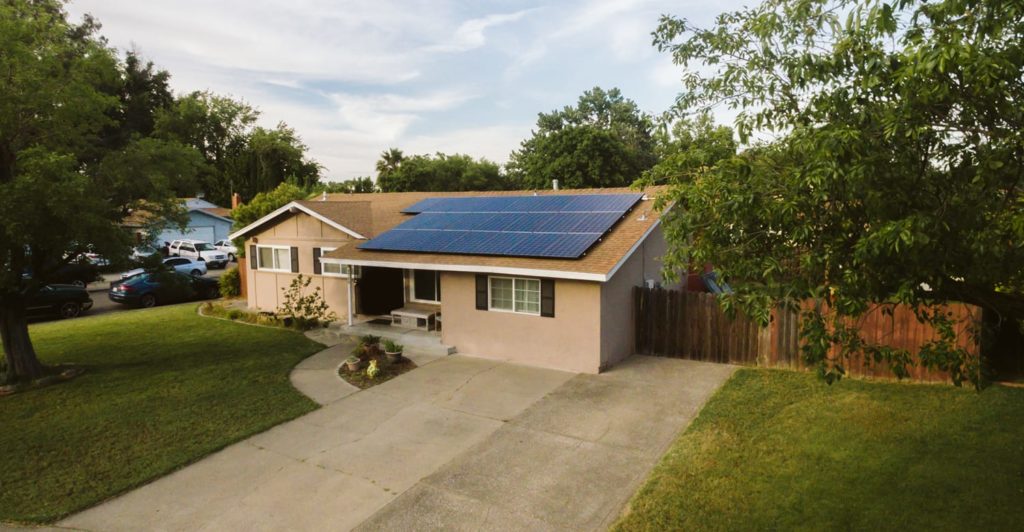Are solar panels reliable on this modern home with solar panels installed on the roof, surrounded by greenery.